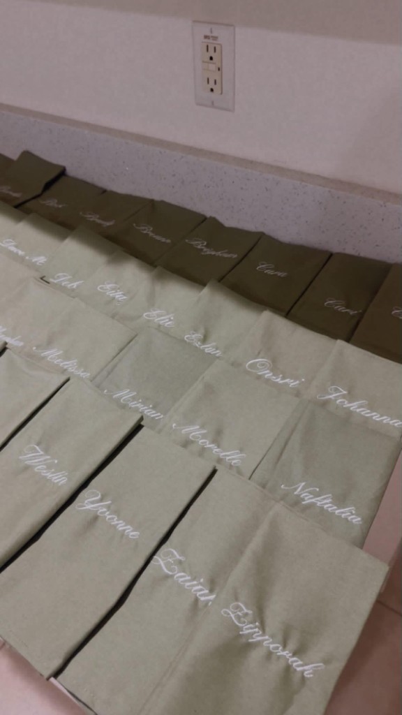 Rows of sage fabric pieces each embroidered with a different name in white script