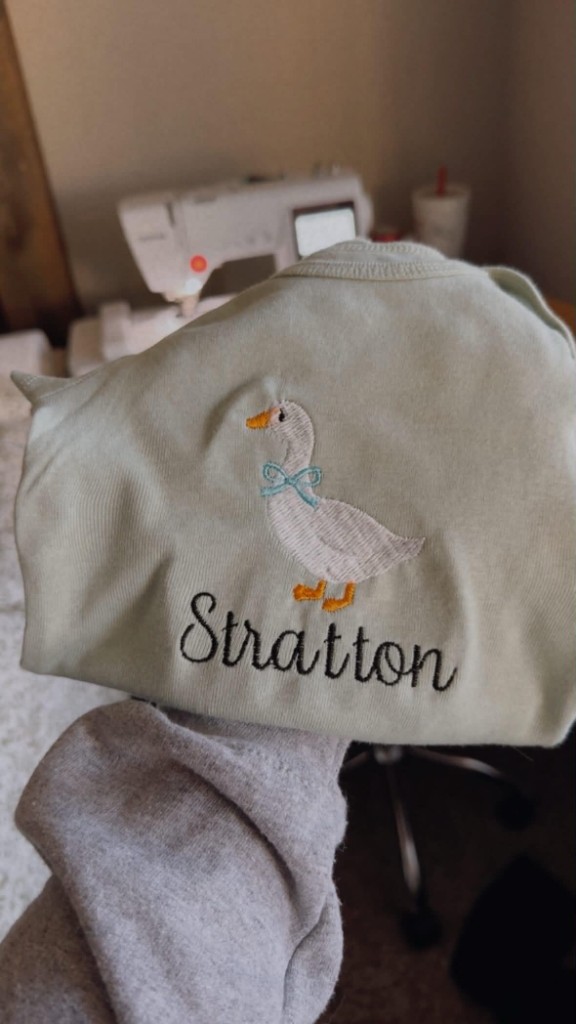 Sage baby onesie with white duck embroidery and the name Stratton