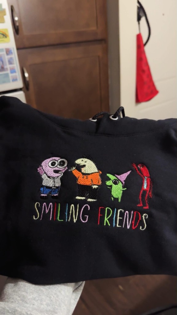 Black hoodie with colorful Smiling Friends character embroidery